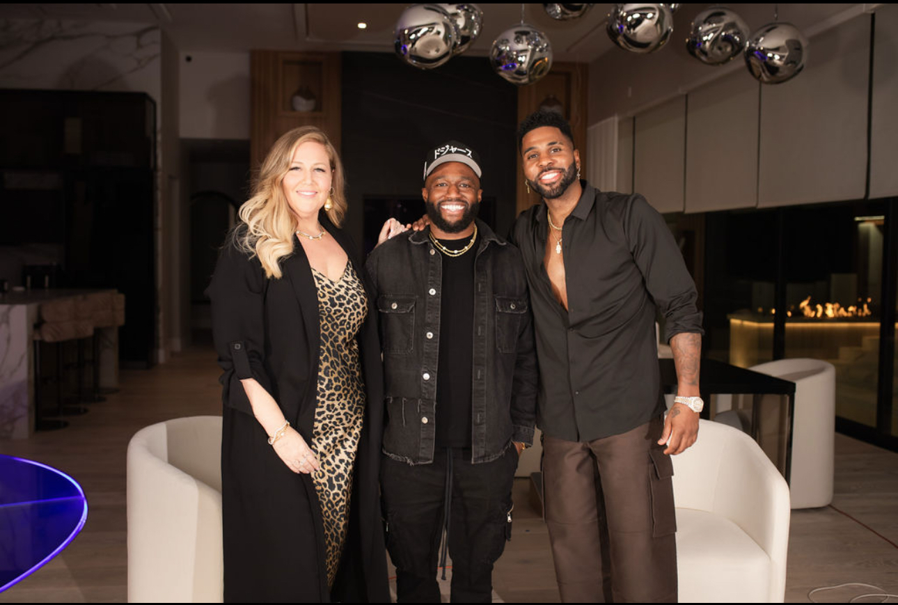Three people in dark outfits smiling together in a modern lounge with white chairs and silver pendant lights