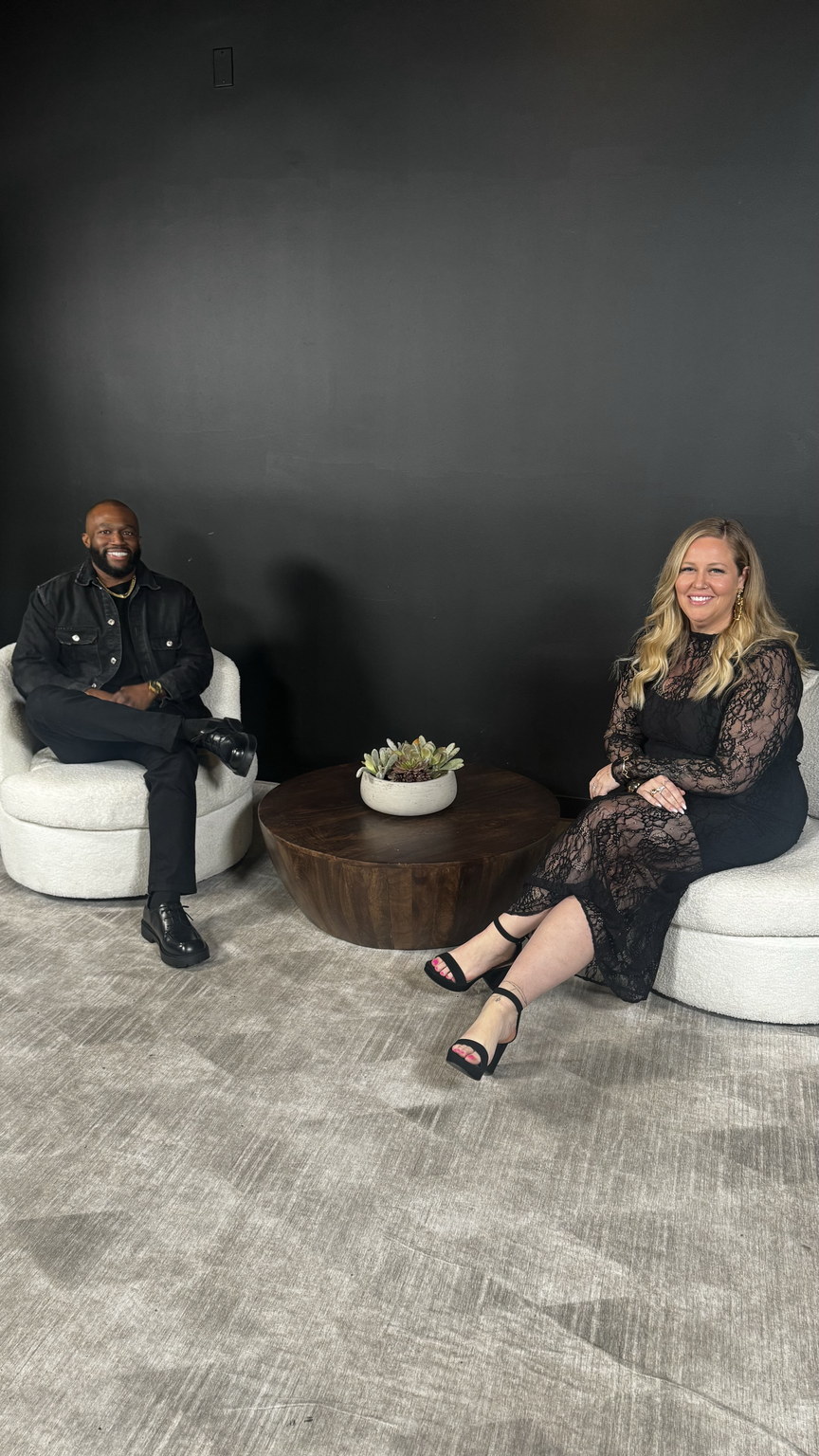 Two people seated in white armchairs for an interview-style conversation against a dark wall